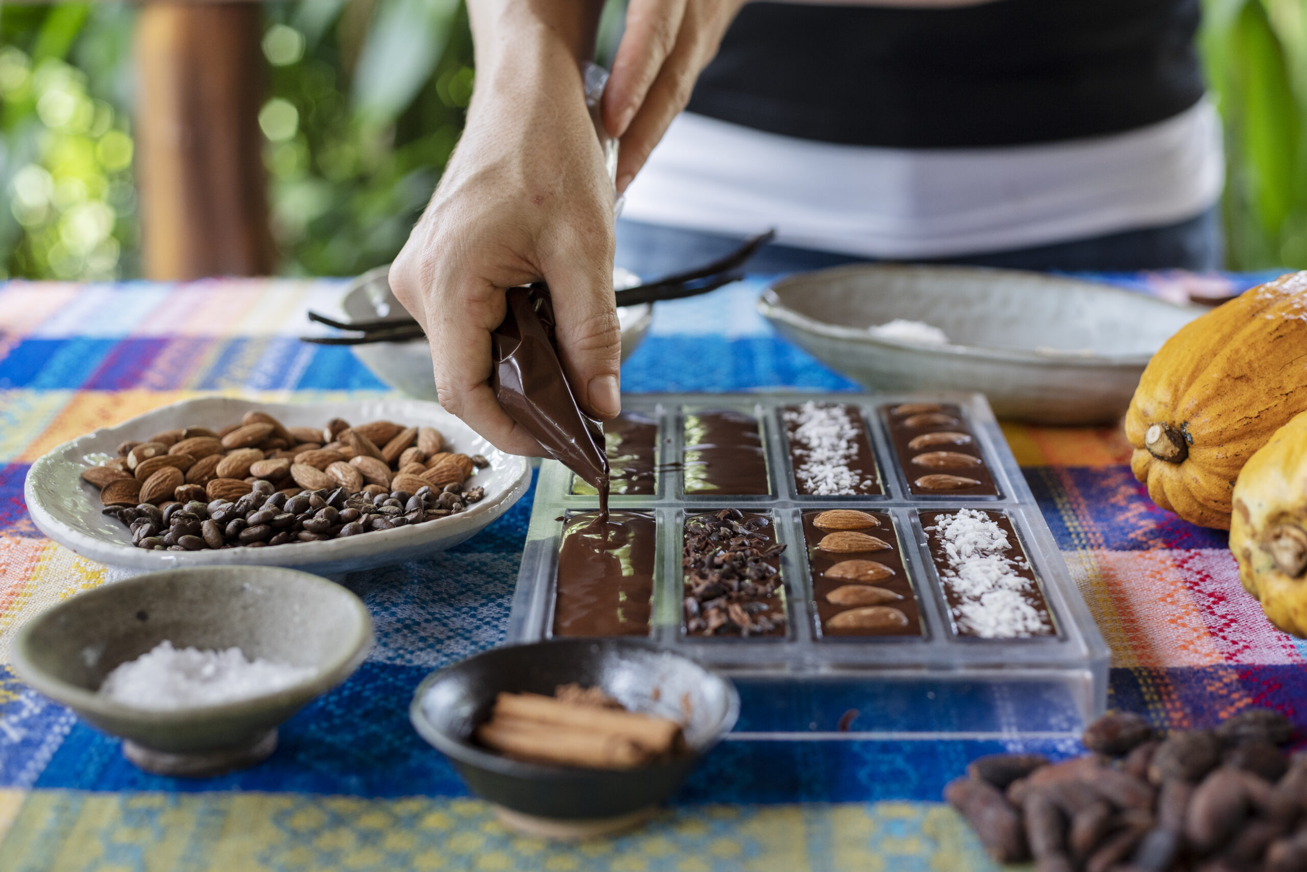 Pouring melted dark chocolate into artisan molds with roasted ingredients