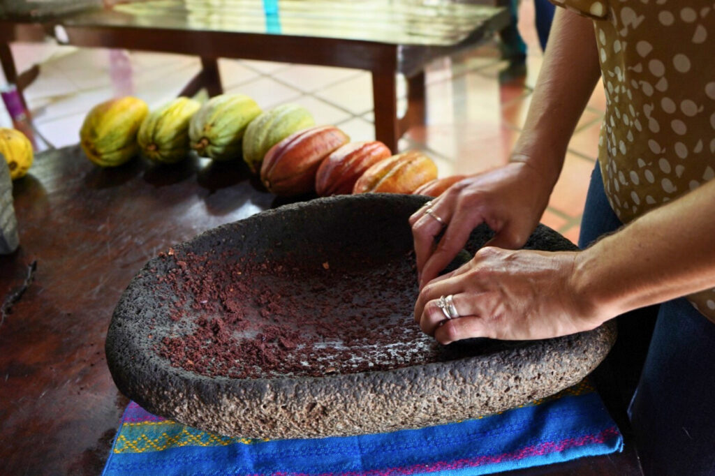 Hands grinding roasted cacao on a traditional volcanic stone metate