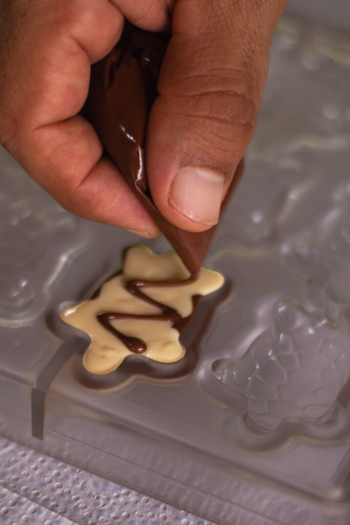 Piping melted chocolate into a decorative mold by hand