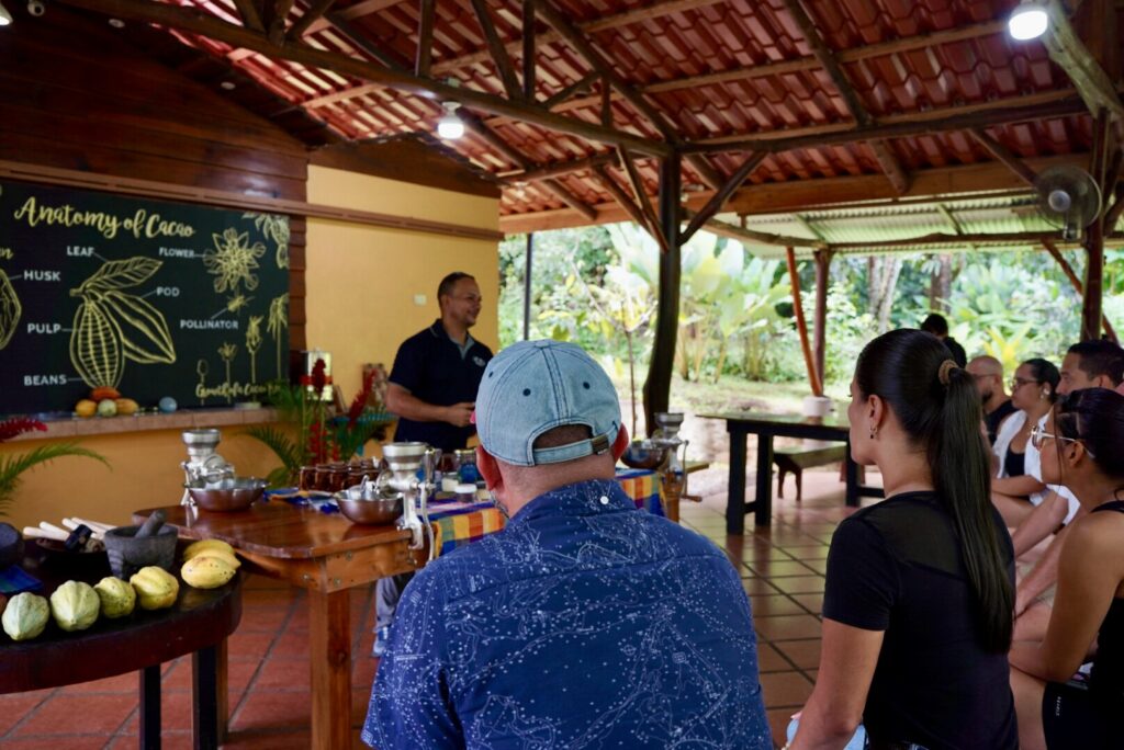 A guide teaching the anatomy of cacao to a group of guests using a chalkboard diagram