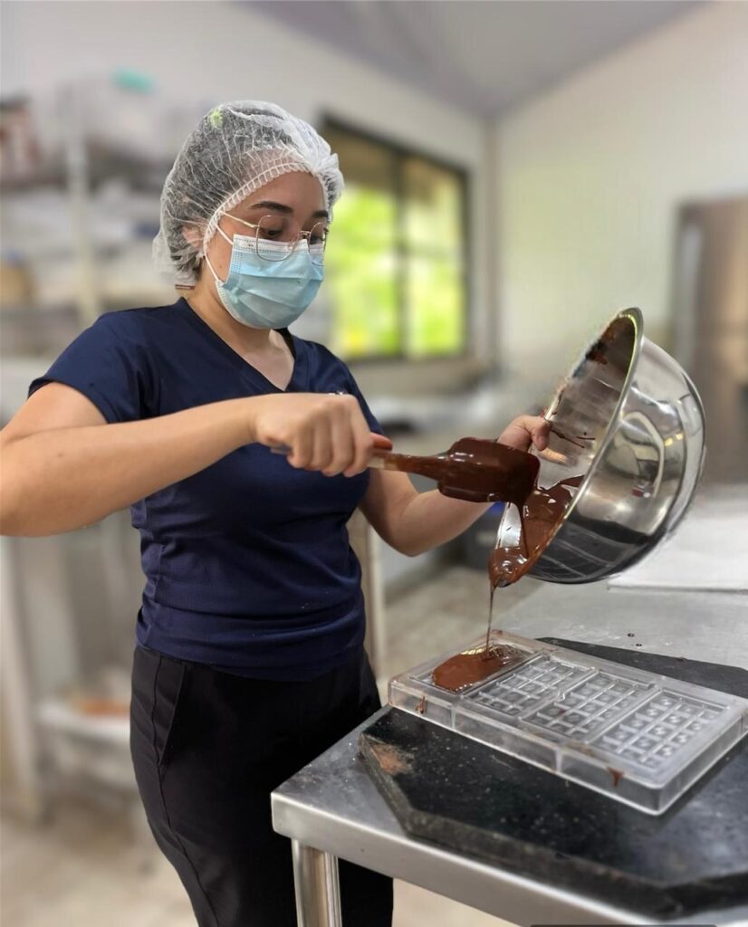 A chocolate maker pouring melted chocolate into a bar mold