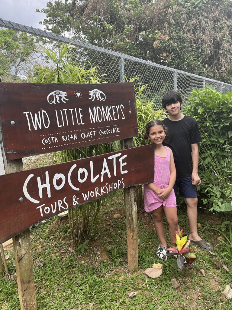 Two children standing beside the Two Little Monkeys chocolate tours and workshops sign